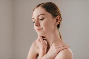 Confident in her skin. Portrait of beautiful young woman with freckles on face looking away and keeping hands on shoulders photo