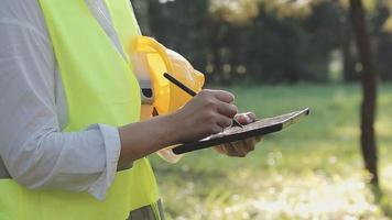 smart asiatisk arbetstagare man eller manlig civil ingenjör med skyddande säkerhet hjälm och reflekterande väst använder sig av digital läsplatta för projekt planera och kontroll arkitektonisk teckning på konstruktion webbplats. video