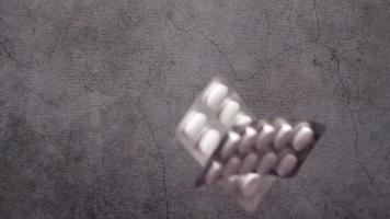 Foil pill packs fall in slow motion onto gray concrete textured surface video