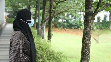 Woman stands on outdoor pathway wearing hijab and face mask video