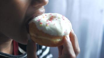 jeune prend une bouchée d'un beignet glacé avec arrose video