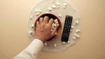 Hand grabbing popcorn from a bowl and a remote control video