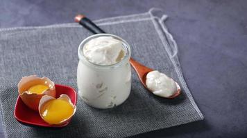 Plain yogurt in jar and wooden spoon and egg yolks in eggshell video