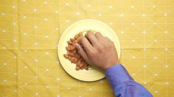 Adult hands reach down and grab two handfuls of almonds from a yellow plate video