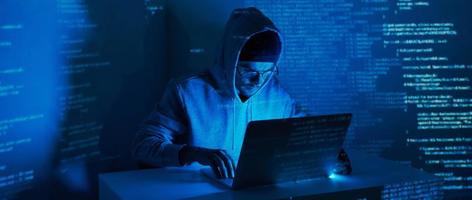 Young man in hooded shirt using computer against dark background photo