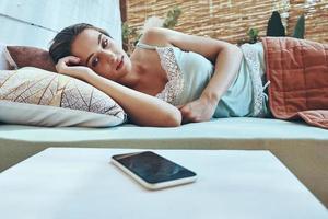 Beautiful young woman looking at mobile phone while lying down in domestic bed