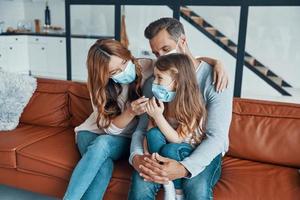 Young family with preschool age girl wearing protective face masks while bonding together at home photo