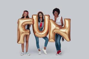 Full length of three attractive young women carrying balloons and smiling while standing against grey background photo