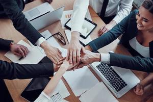 Top view of cheerful business team keeping hands together as a symbol of unity while working together in the modern office photo