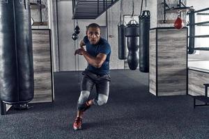 Pushing himself to the limit. Full length of handsome young African man in sport clothing running while exercising in the gym photo