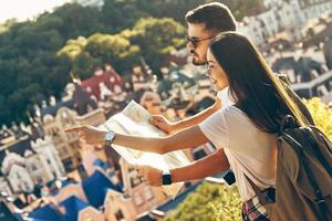 curioso joven pareja de turistas examinando el mapa y sonriendo mientras está de pie al aire libre foto