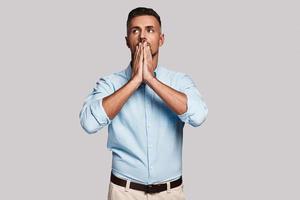 Despair. Frustrated young man covering mouth with hands while standing against grey background photo