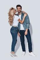 Totally in love. Full length of beautiful young couple kissing and smiling while standing against grey background photo