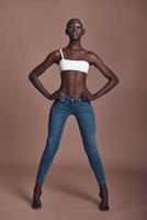 Fashion model. Full length of attractive young African woman looking at camera and keeping hands on hips while standing against brown background photo