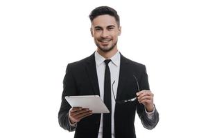 Confident advisor. Handsome young man in full suit holding digital tablet and smiling while standing against white background photo