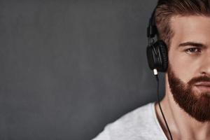 Music is his motivation.  Close up of good looking young man half face listening music while standing against grey background photo