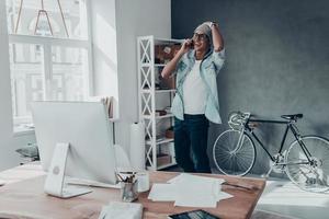 Handsome young man in eyewear talking on smart phone and smiling while standing in creative office photo