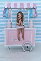 niña feliz. linda niñita con las manos juntas y sonriendo mientras se sienta en la decoración del carrito de dulces foto