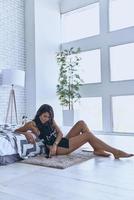 Choosing the right song.  Thoughtful young woman in panties wearing headphones and using her smart phone while sitting on the floor at home photo