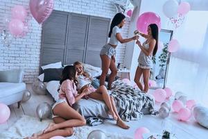 tiempo de calidad con amigas. cuatro jóvenes sonrientes juguetonas en pijama uniéndose mientras pasan tiempo en el dormitorio con globos por toda la habitación foto