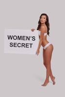 Every woman got it.  Full length of attractive young woman holding a poster and looking at camera while standing against grey background photo