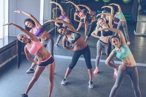 Aerobics with girls. Young beautiful cheerful women with perfect bodies in sportswear exercising and looking at camera with smile at gym photo