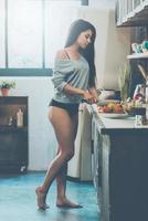 Beauty in kitchen. Full length of beautiful young mixed race woman cutting vegetables for salad while standing in kitchen at home photo