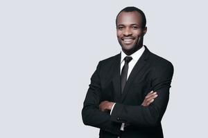 Confidence and style. Handsome young African man in formalwear keeping arms crossed and looking at camera while standing against grey background photo