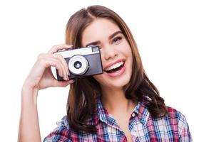 Expert in photography. Cheerful young woman holding camera and making photo while standing against white background