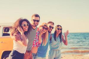 Enjoying freedom. Group of cheerful young people embracing and looking at camera while walking along the beach photo