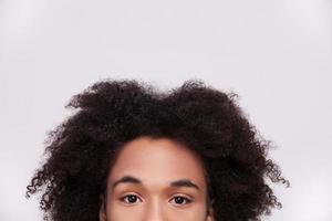 Candid look. Cropped image of cheerful African teenager looking at camera while isolated on grey background photo