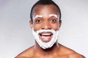 Shaving is fun. Portrait of playful African man with shaving cream beard and mustache smiling at camera while standing against grey background photo