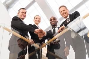 Strong business team. Low angle view of four confident business people standing close to each other and holding hands together photo