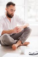 Financial problems. Depressed young man looking at the paper and holding hands on chin while sitting on the floor at his apartment photo