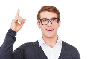 The birth of new idea. Cheerful young man pointing up and smiling at camera while standing isolated on white photo