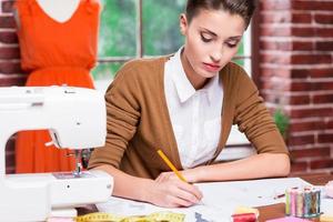 diseñador de moda creativo. bella joven dibujando bocetos de moda mientras se sienta en su lugar de trabajo foto