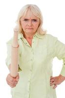 Senior woman with rolling pin. Angry senior woman holding rolling pin and looking at camera while standing isolated on white background photo