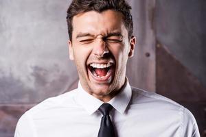 Stressed businessman. Furious young man in shirt and tie shouting and keeping eyes closed photo