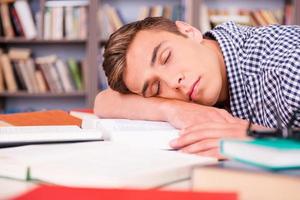 durmiendo en la biblioteca. apuesto joven durmiendo mientras está sentado en la biblioteca y apoyando su rostro en el escritorio foto