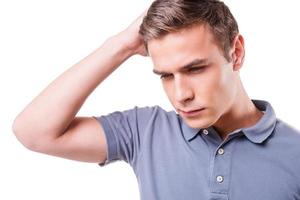 Failed again. Depressed young man holding hand in hair and looking down while standing isolated on white background photo
