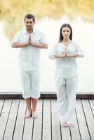 encontrar la paz juntos. toda la longitud de una hermosa pareja joven vestida de blanco meditando juntos al aire libre foto