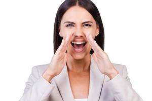 Announcing good news. Happy young businesswoman in suit shouting and holding hands over mouth while standing against white background photo