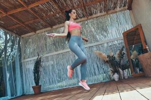 Full length of beautiful young woman in sports clothing using jumping rope on patio photo