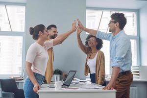 Group of young business people in smart casual wear holding hands together and smiling photo