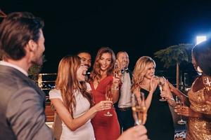 grupo de personas en ropa formal comunicándose y sonriendo mientras pasan tiempo en una fiesta de lujo foto