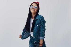 Attractive young woman in eyewear and bandana smiling while standing against grey background photo