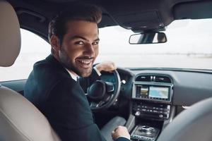 Ready to go Handsome young man in full suit looking at camera and smiling while driving a car photo