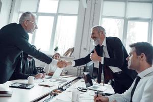 Modern businessmen shaking hands while working together with their team in the office photo