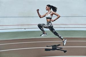 llena de energía. toda la longitud de una mujer joven con ropa deportiva corriendo mientras hace ejercicio al aire libre foto