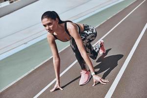 Ready to overcome any obstacle. Beautiful young woman in sports clothing standing on the start line while exercising outdoors photo